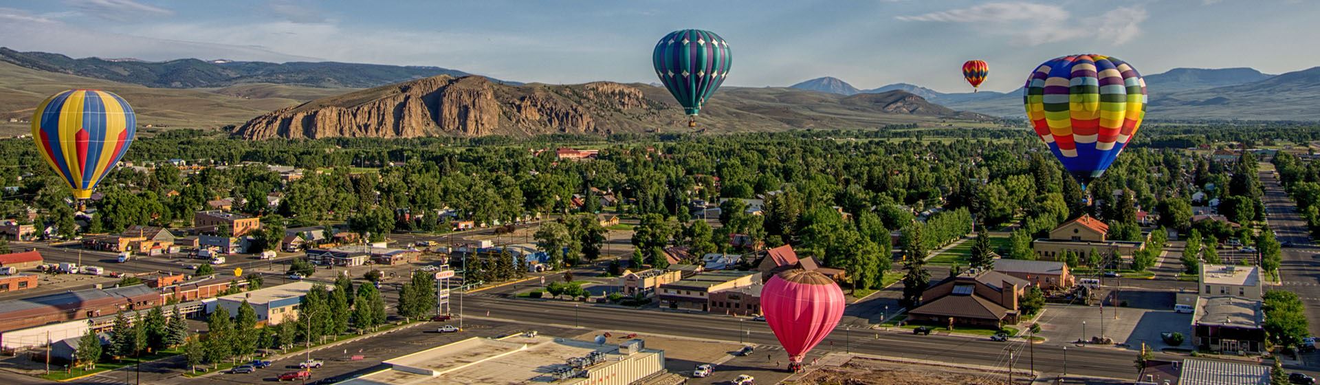 Hot air balloons in the sky over a town with mountains in the back ground